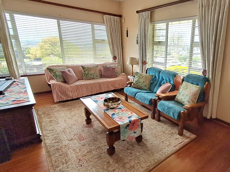 A living room featuring timber flooring and large windows with venetian blinds, offering natural light and views.