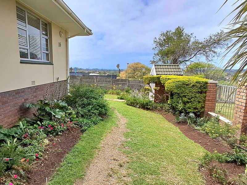 A well-maintained side garden featuring established landscaping, brick boundary walls, and a small decorative garden structure with a tiled roof.