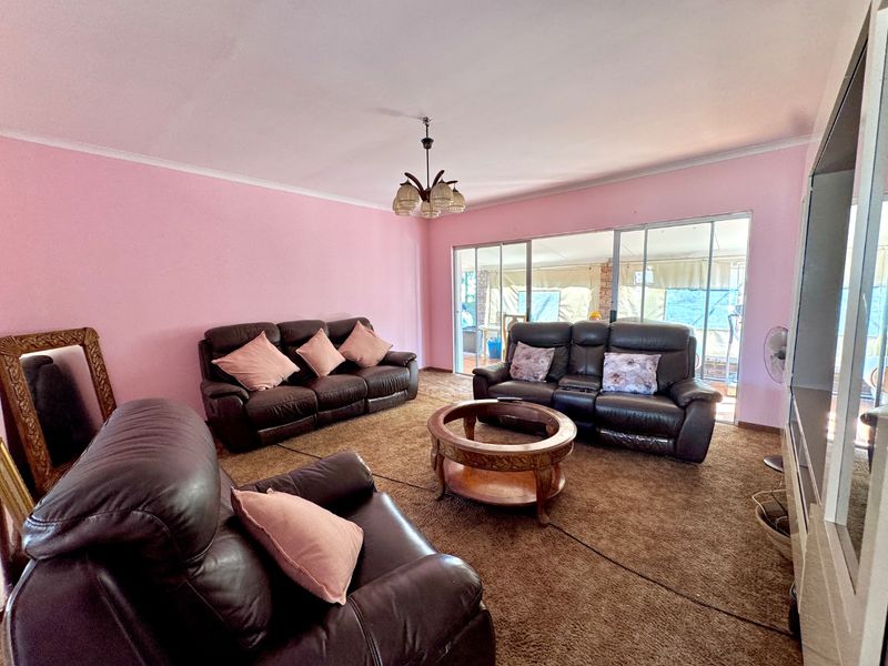 Spacious living room featuring pink walls, brown carpeting, and large sliding glass doors providing access to the outdoor area.