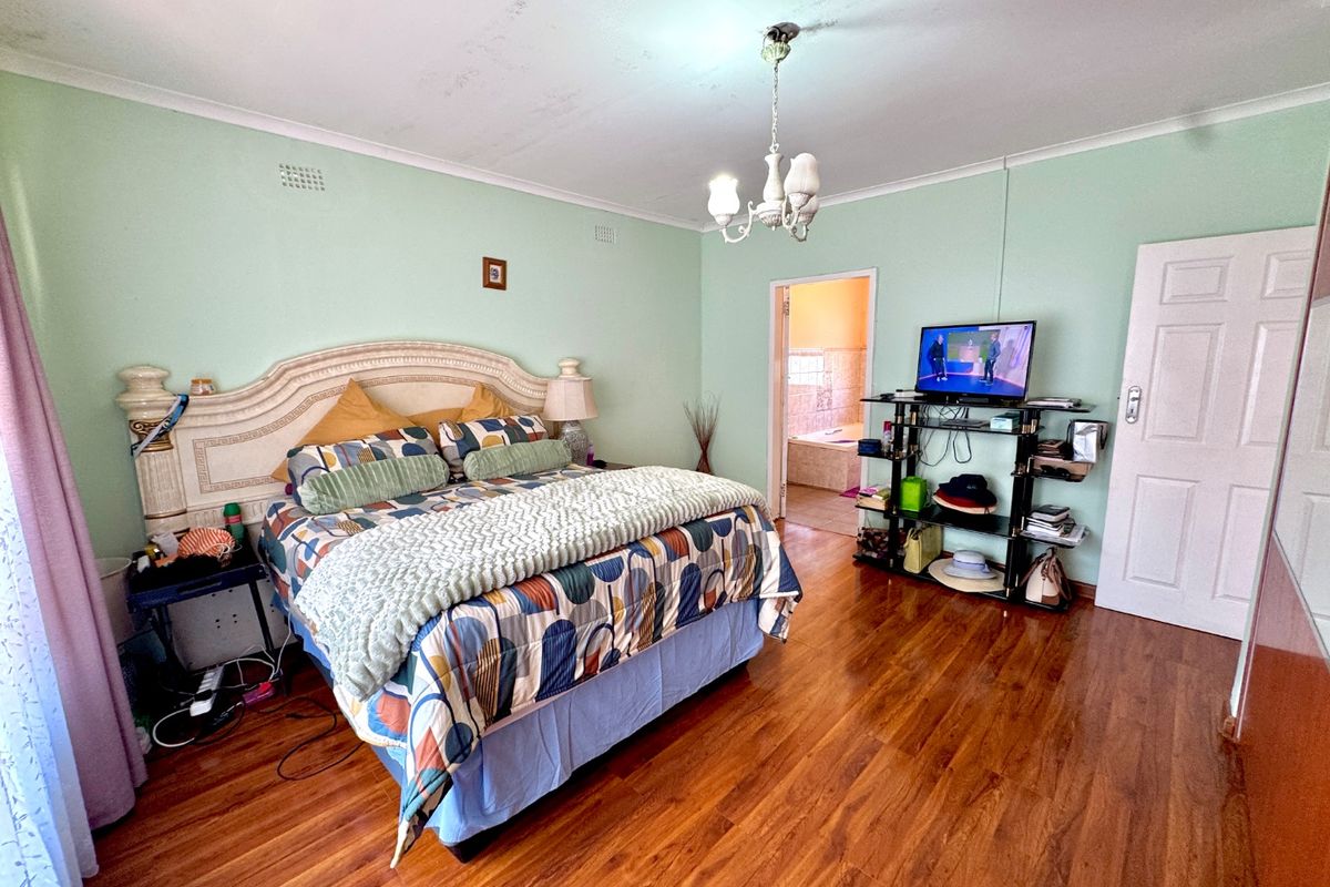 Spacious bedroom featuring laminate flooring and direct access to an en-suite bathroom, requiring ceiling repairs and cosmetic updates.