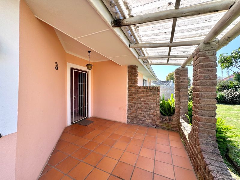 Covered patio area featuring terracotta tiling, exposed brick pillars, and a translucent roof structure, providing a sheltered outdoor entrance space.