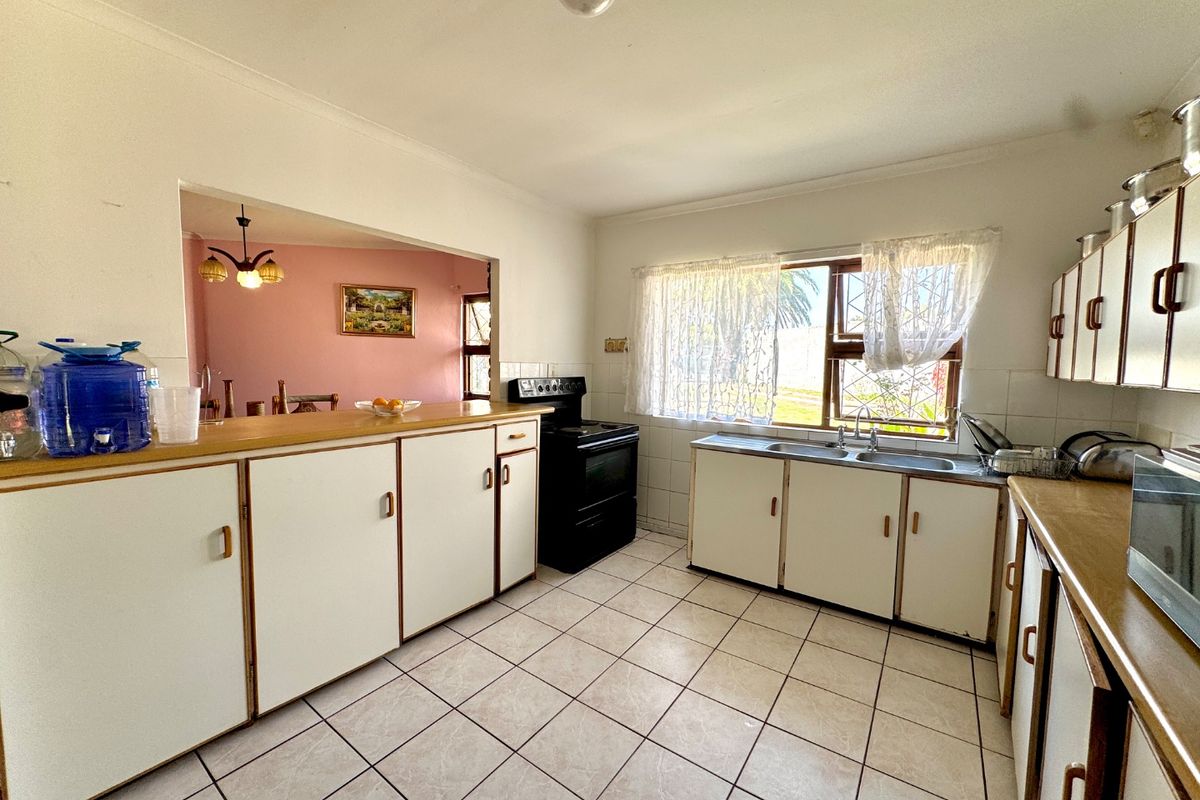 A functional kitchen featuring white built-in cabinetry, laminate countertops, a double basin sink, and a freestanding stove, with tiled flooring throughout.