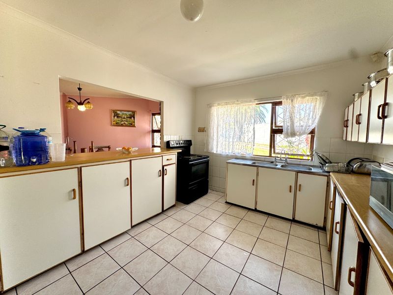 A functional kitchen featuring white built-in cabinetry, laminate countertops, a double basin sink, and a freestanding stove, with tiled flooring throughout.
