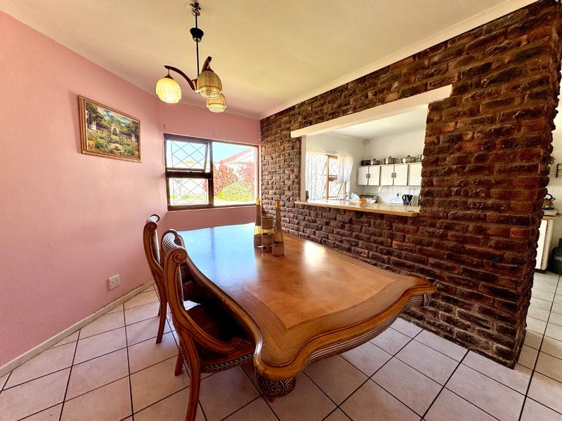 Dining room featuring an exposed brick wall with a serving hatch connecting to the kitchen, tiled flooring, and natural light from the window.