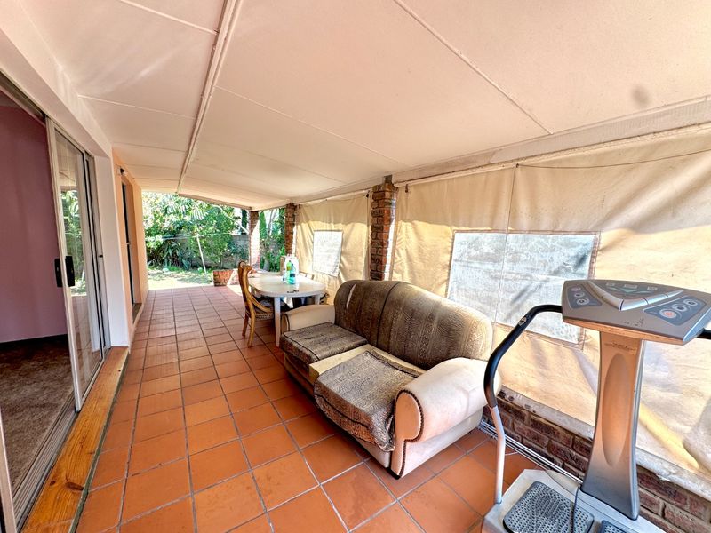 A covered patio area featuring tiled flooring, exposed brick pillars, and roll-up canvas blinds, providing a functional outdoor living space.