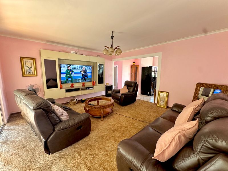 A spacious living room featuring a built-in media unit, carpeted flooring, and a central light fixture, offering a functional layout for relaxation.