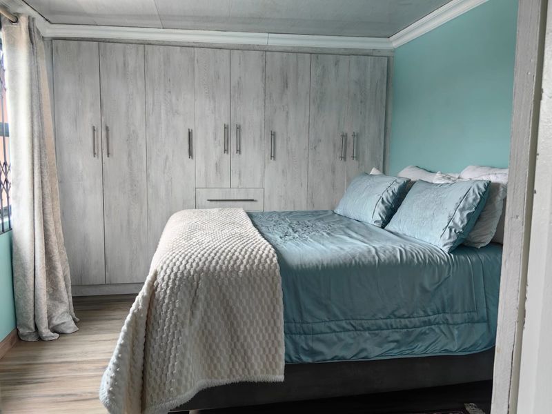 A well-maintained bedroom featuring extensive built-in cupboards with a wood-grain finish, laminate flooring, and decorative ceiling cornicing.