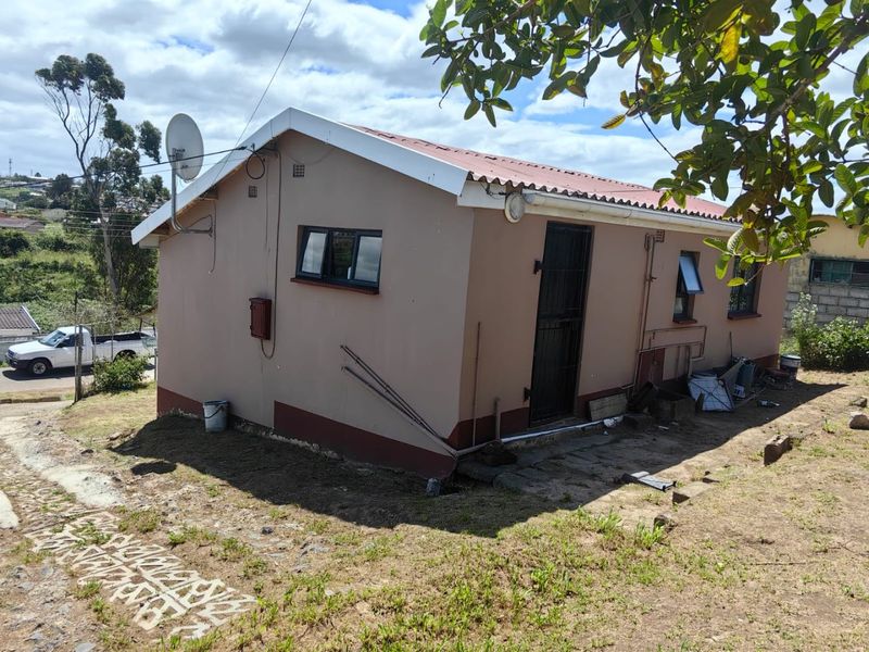 Rear view of a detached house featuring a corrugated metal roof, security gate, and basic exterior finishes on a sloped plot.