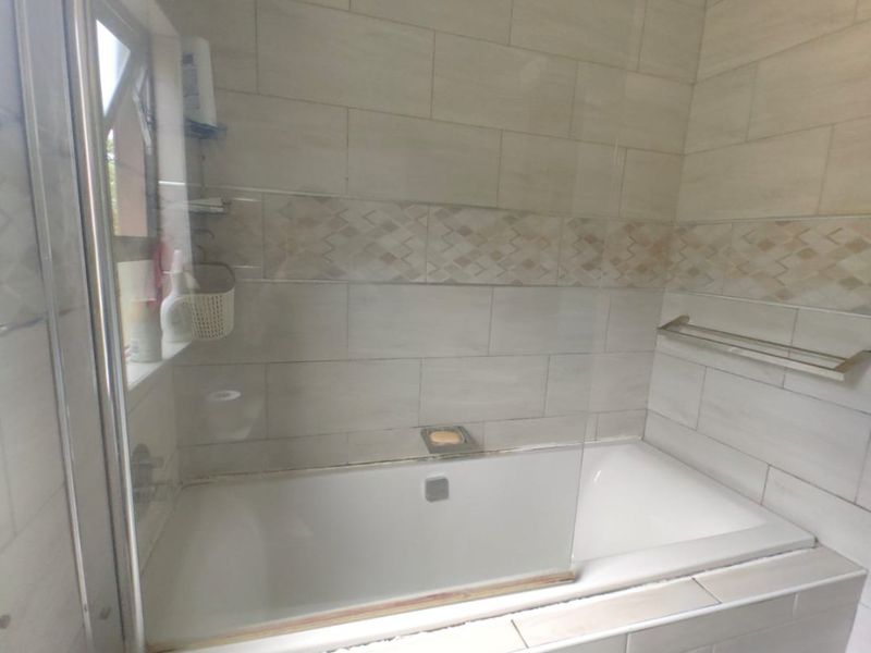A bathroom featuring a built-in bathtub with a glass shower screen, overhead shower, and neutral tiled finishes.