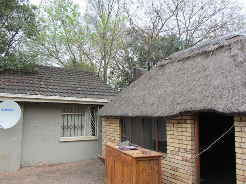 Rear exterior view showing a combination of a thatched roof structure and a tiled roof building with paved courtyard area.