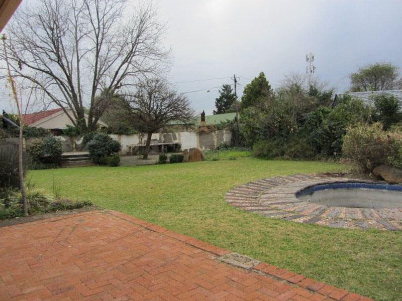 Rear garden featuring a brick paved patio, a lawn area, and an in-ground swimming pool with a brick surround.