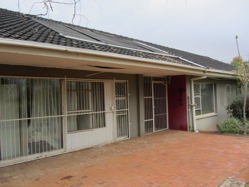 Rear exterior view of the house featuring a brick paved patio, security gates, and a solar water heating panel on the tiled roof.