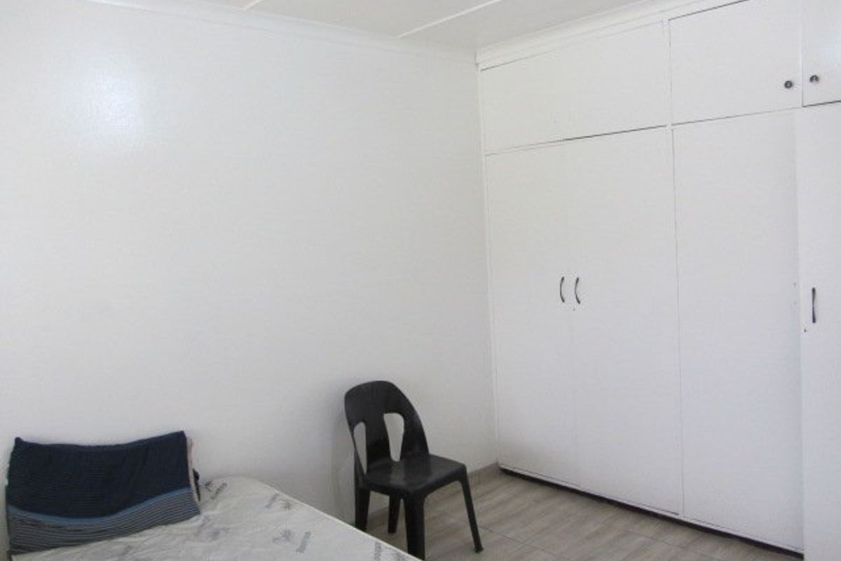 A simple bedroom featuring neutral tiled flooring and white built-in cupboards, offering a clean and functional space ready for personalization.