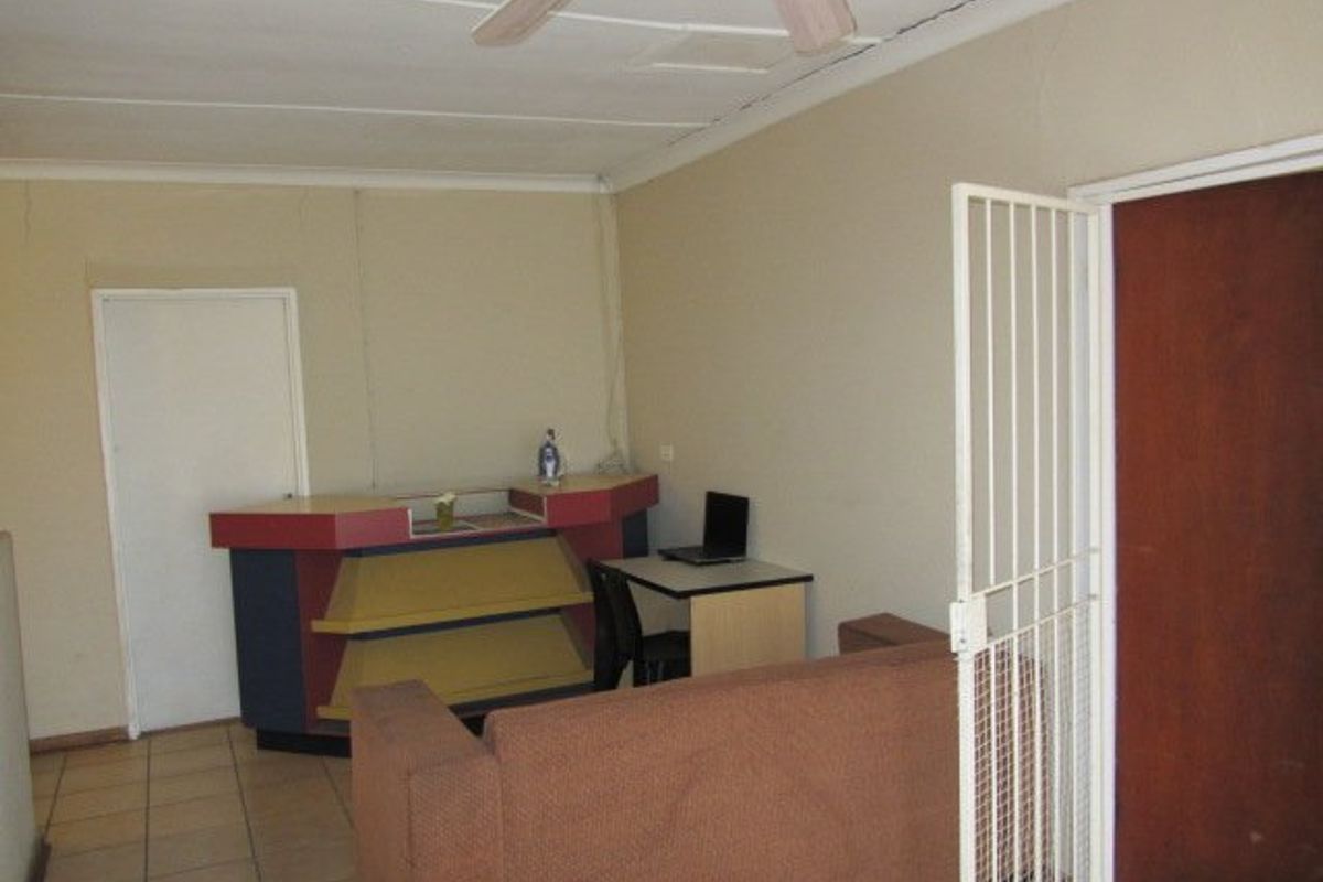 A living area featuring tiled flooring, a ceiling fan, and a security gate, requiring cosmetic updates to improve its overall appeal.