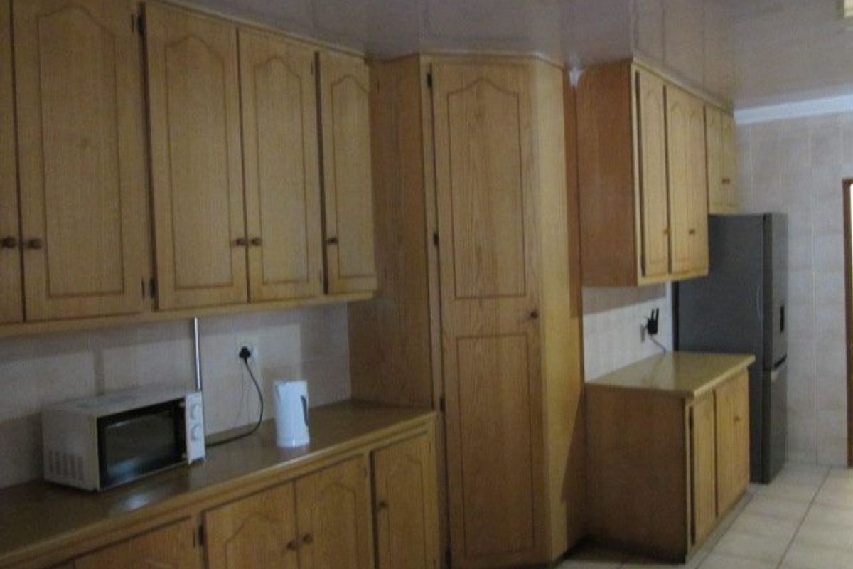 A functional kitchen featuring extensive built-in wooden cabinetry, laminate countertops, and tiled flooring, offering ample storage space for culinary needs.
