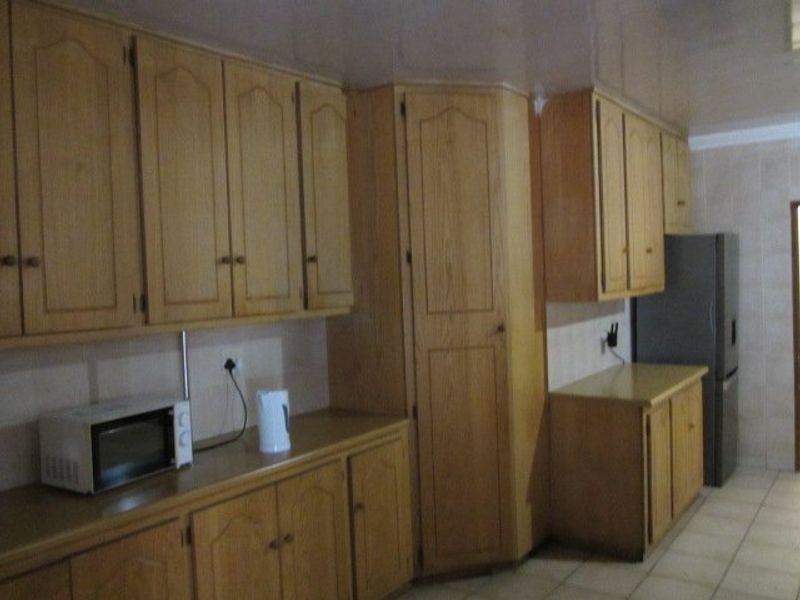 A functional kitchen featuring extensive built-in wooden cabinetry, laminate countertops, and tiled flooring, offering ample storage space for culinary needs.