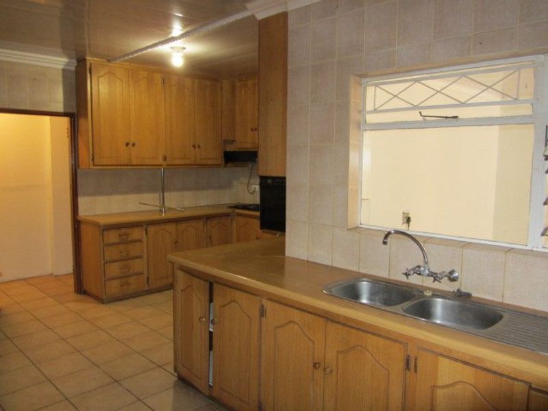 A dated kitchen featuring wooden cabinetry, a double bowl sink, tiled backsplash, and built-in oven, offering a functional layout ready for modernization.