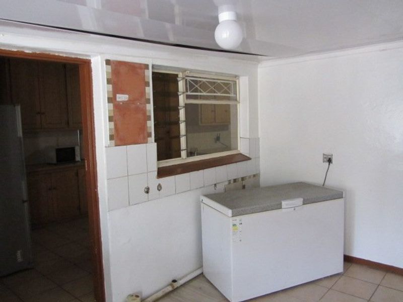 A functional scullery or utility area featuring tiled flooring, a window with security bars, and exposed plumbing, requiring cosmetic updates to improve the finish.