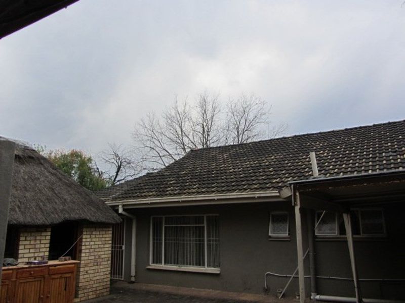 Rear view of the property showing a main house with tiled roofing and an adjacent thatched structure, featuring weathered finishes and security window bars.