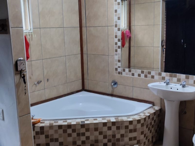 A functional bathroom featuring a corner bathtub, pedestal basin, and toilet with neutral tiled finishes and a large wall-mounted mirror.