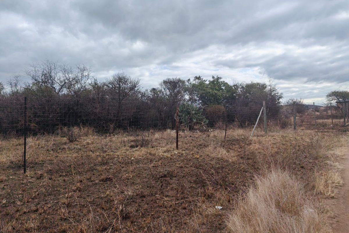 A view of a vacant residential plot featuring dry vegetation and existing wire mesh perimeter fencing with some signs of wear.