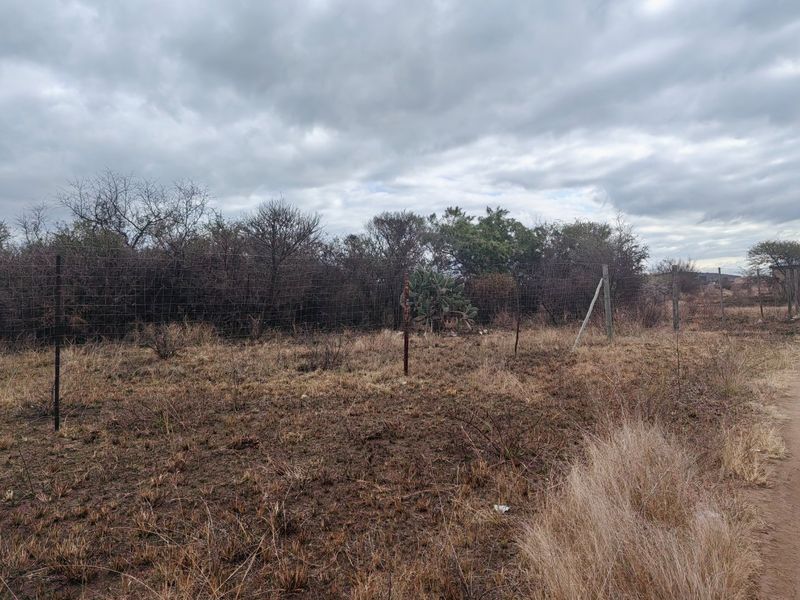 A view of a vacant residential plot featuring dry vegetation and existing wire mesh perimeter fencing with some signs of wear.
