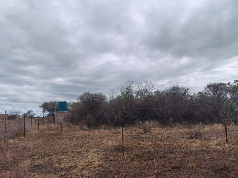 A view of the vacant residential land featuring wire mesh fencing, a masonry boundary wall, and a water storage tank.