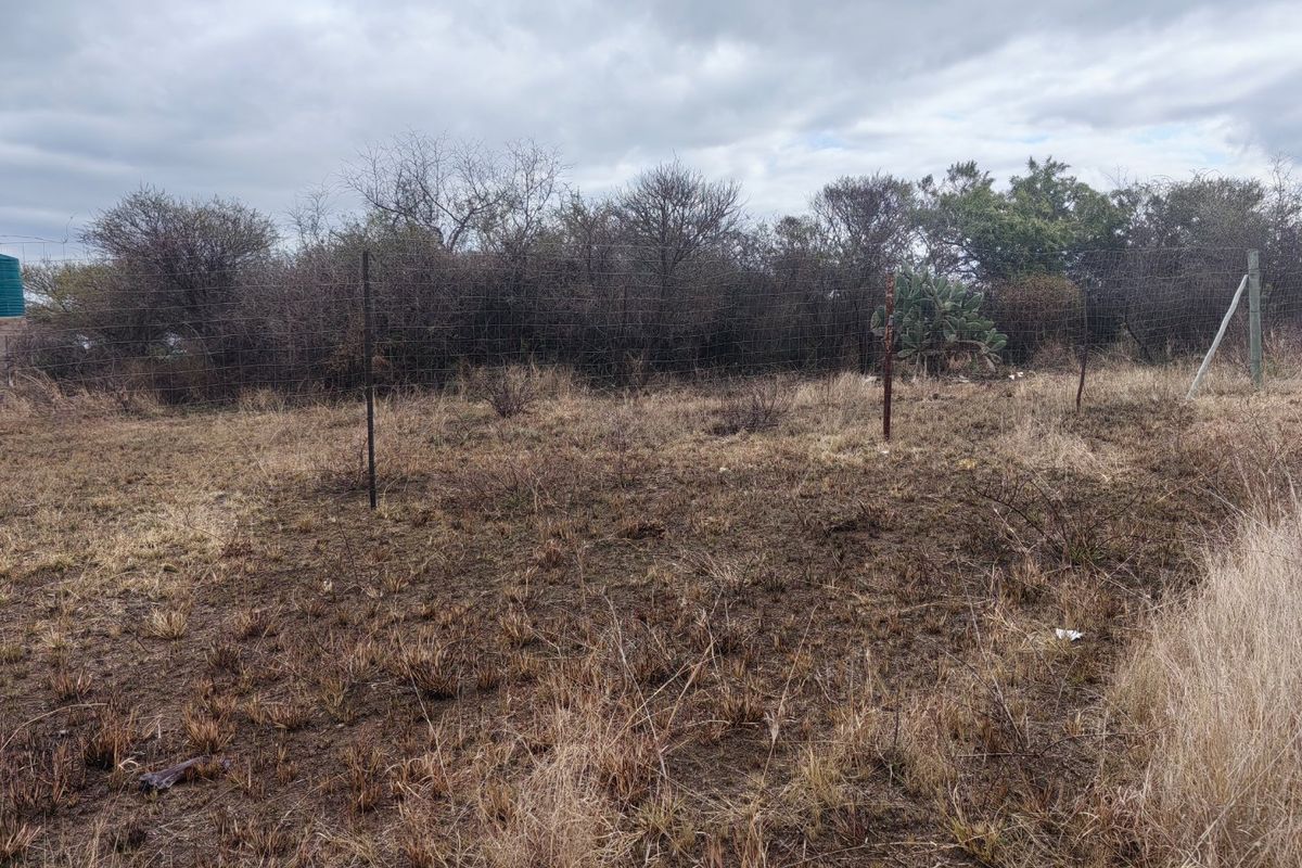 A view of the vacant residential land featuring dry grass and perimeter wire mesh fencing with metal posts.