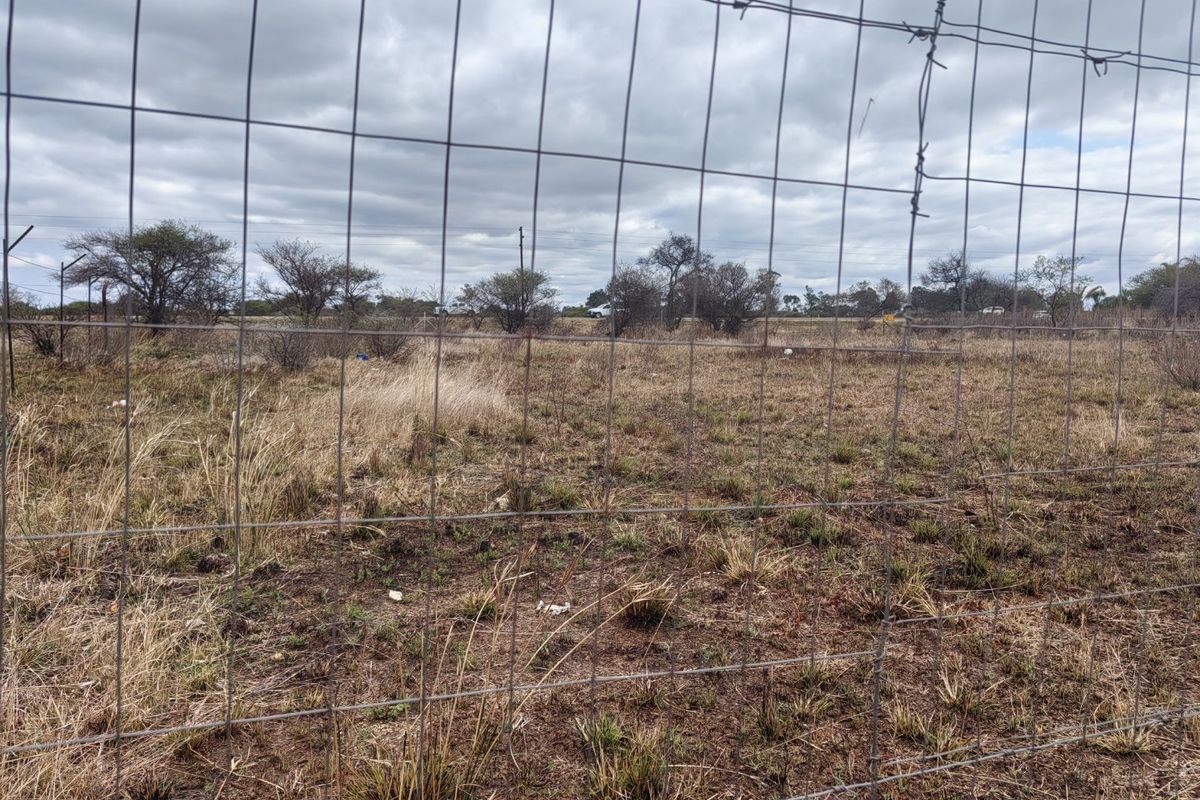 A view of a vacant residential plot enclosed by wire mesh fencing with native vegetation and scattered trees.