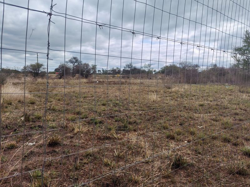 A view of a vacant residential plot enclosed by wire mesh fencing with barbed wire topping.