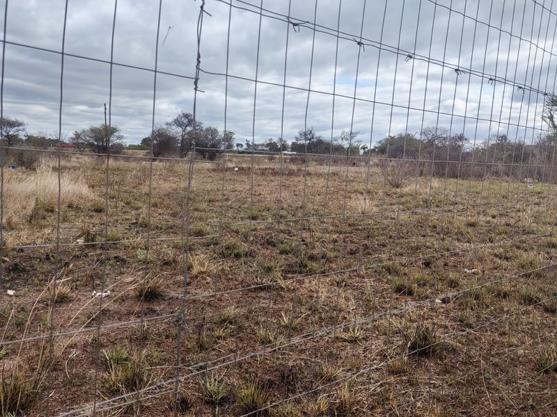 A view of a vacant residential plot enclosed by wire mesh fencing with barbed wire topping.