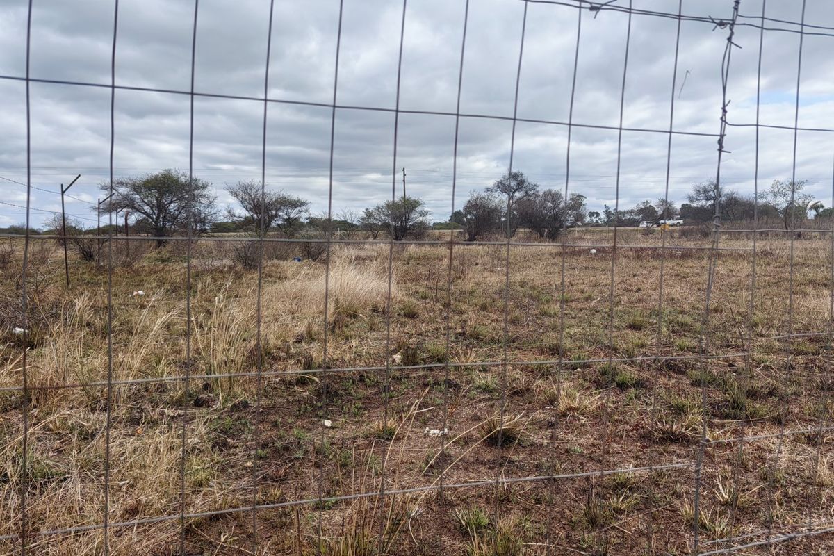 A view of a vacant residential plot enclosed by wire mesh fencing with native vegetation and scattered trees.