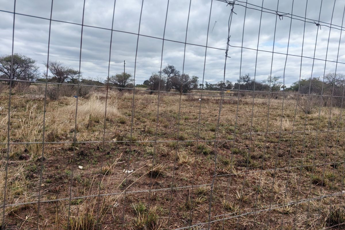 A view of a vacant residential plot enclosed by wire mesh fencing with barbed wire topping.