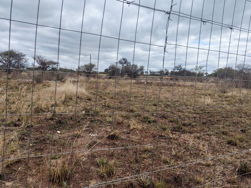 A view of a vacant residential plot enclosed by wire mesh fencing with barbed wire topping.