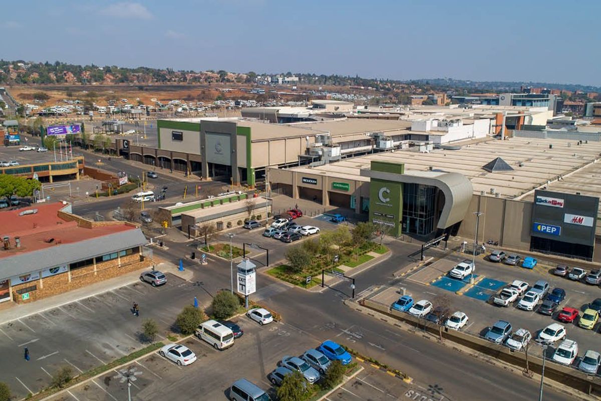 Aerial view of a commercial shopping center complex featuring extensive parking facilities, paved access roads, and modern building architecture.