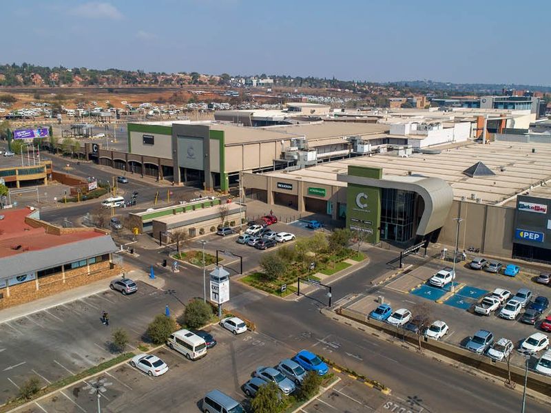 Aerial view of a commercial shopping center complex featuring extensive parking facilities, paved access roads, and modern building architecture.