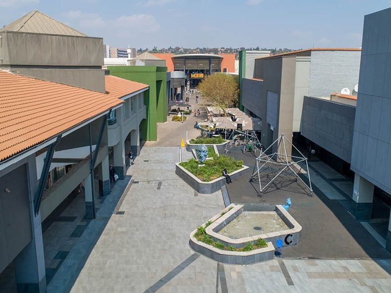 An elevated view of a commercial outdoor courtyard featuring paved walkways, built-in planters, and a central water feature between building wings.
