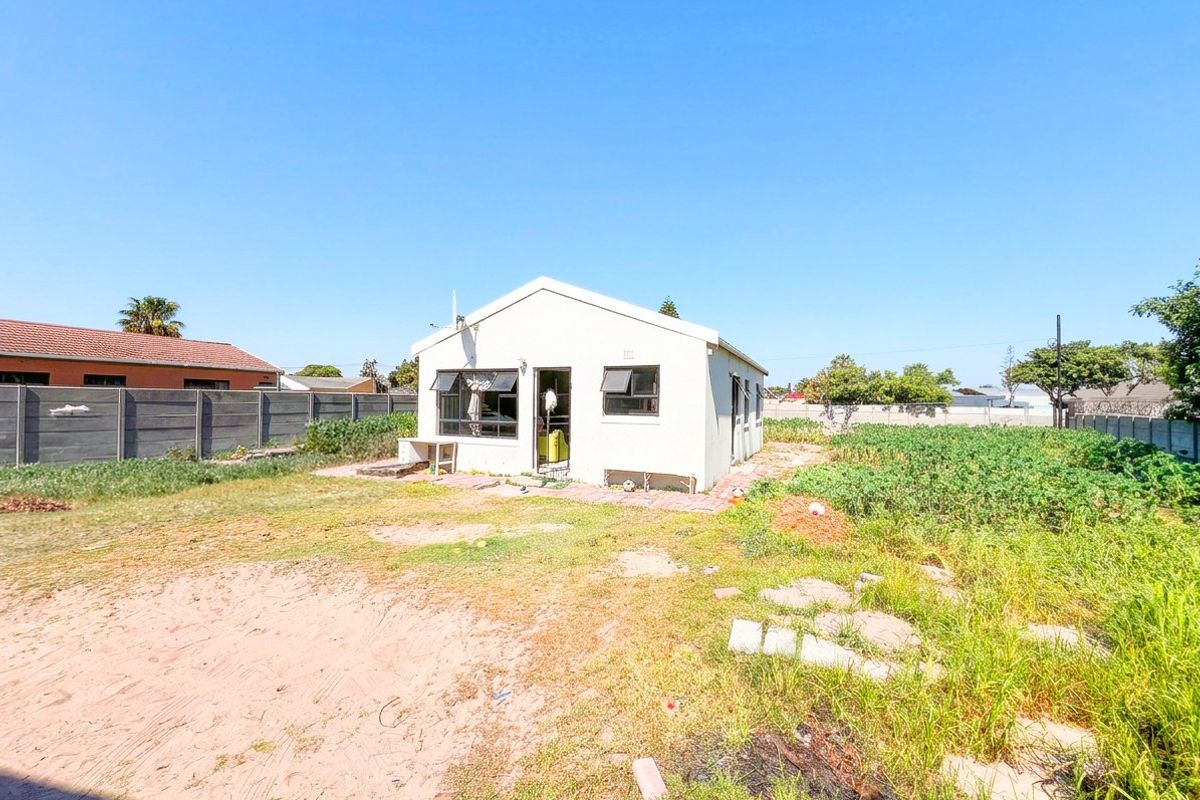 Rear view of a detached house featuring a tiled roof, casement windows, and a large, unmaintained garden area with boundary walling.