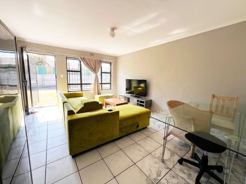 Open-plan living and dining area featuring tiled flooring, security gate access to the exterior, and large windows with fitted burglar bars.
