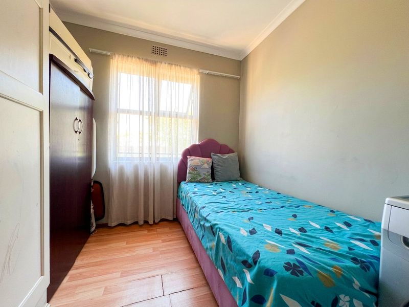 A compact bedroom featuring laminate flooring, a built-in wardrobe, and a window with natural light.