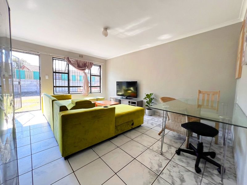 Open-plan living and dining area featuring tiled flooring, security bars on windows, and direct access to the exterior through a glass door.