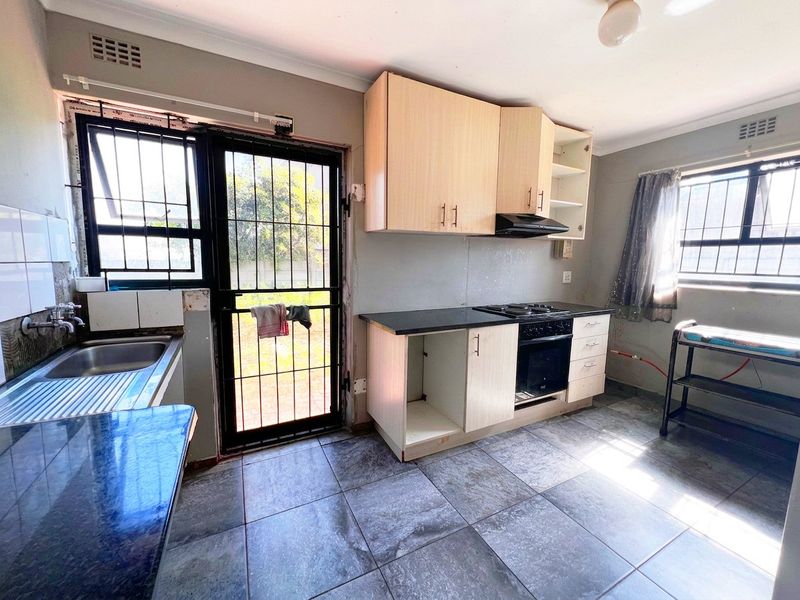 A functional kitchen featuring built-in cabinetry, a built-in oven with hob, and tiled flooring, with direct access to the rear exterior.