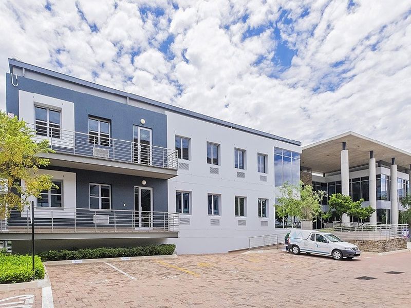 Modern commercial office building featuring a multi-story facade, paved parking area, glass curtain walling, and balconies with metal railings.