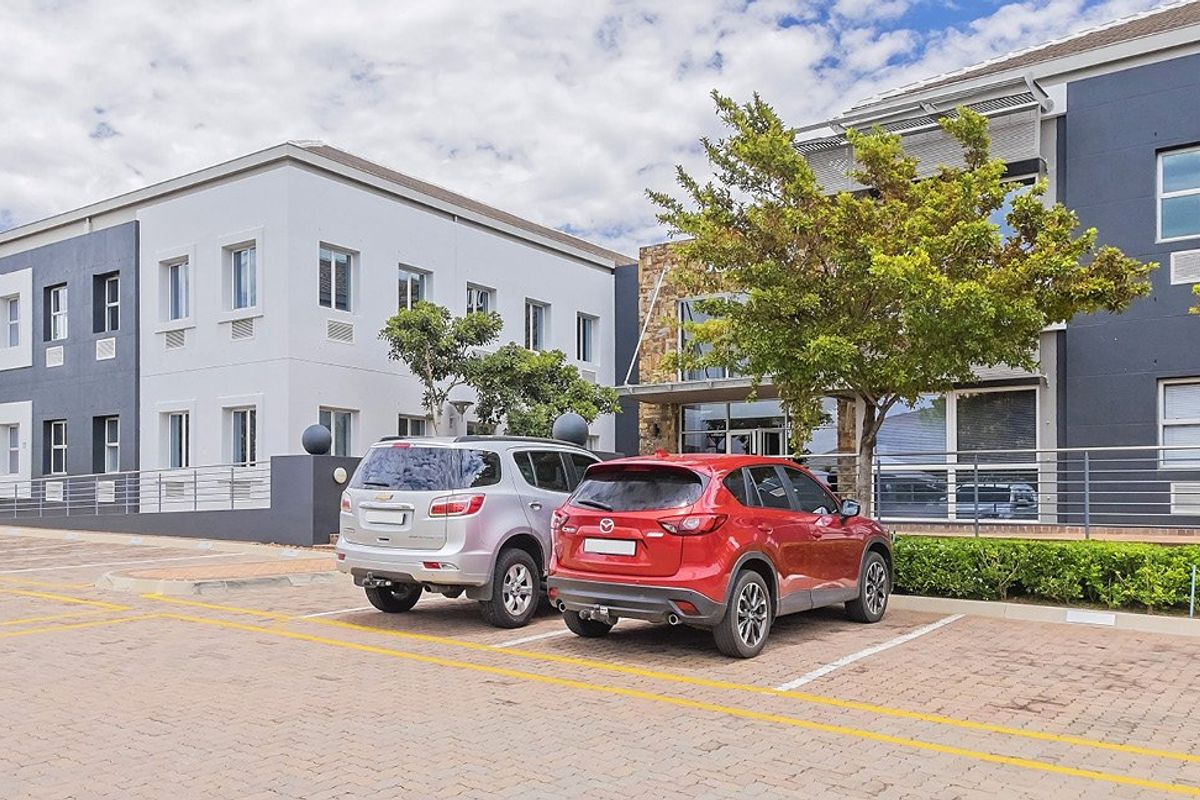 Front exterior view of a modern commercial office building featuring stone cladding, paved parking bays, and metal safety railings.