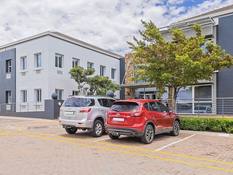 Front exterior view of a modern commercial office building featuring stone cladding, paved parking bays, and metal safety railings.