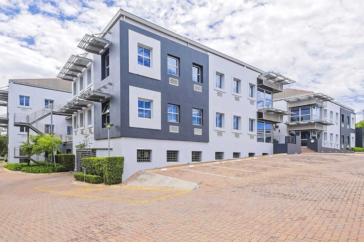 A modern multi-story commercial office building featuring paved parking, external staircases, and contemporary architectural detailing with integrated sunshades and air conditioning units.