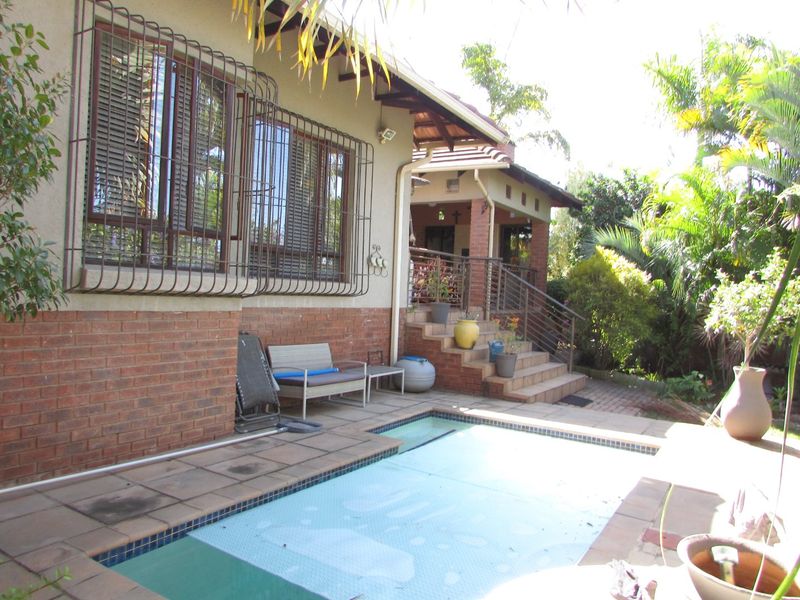 Rear exterior view featuring a swimming pool, brick facade with security bars, and a raised patio area with stairs leading to the home.