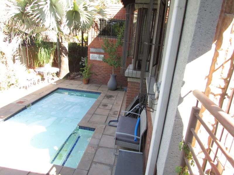 A compact outdoor pool area featuring a paved deck, brick walling, and security bars on the adjacent building windows.