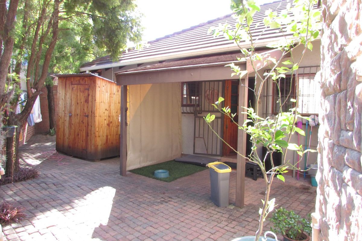 A rear courtyard featuring a paved area, a covered patio space, and a detached wooden storage shed.