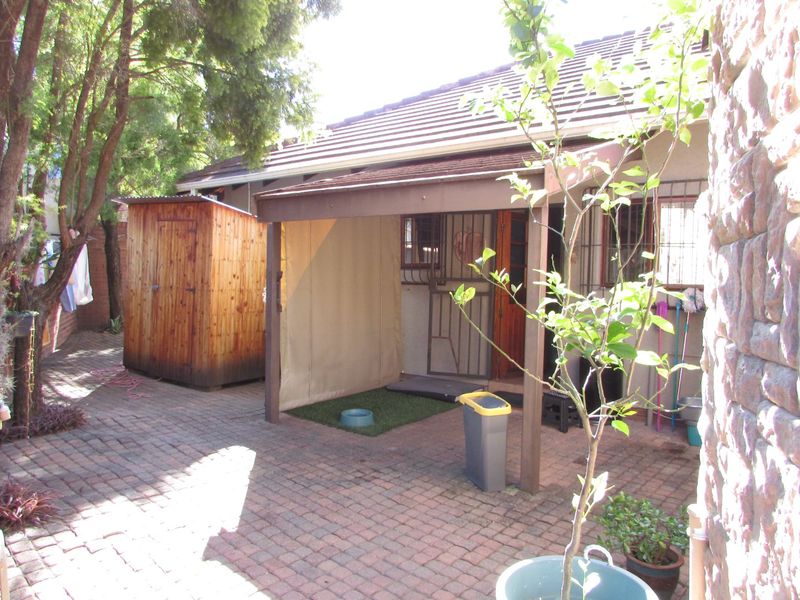 A rear courtyard featuring a paved area, a covered patio space, and a detached wooden storage shed.
